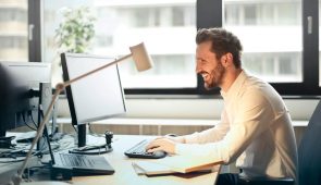image of a man typing on a computer while smiling at the screen